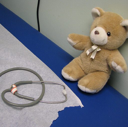 A stethoscope and a teddy bear are close-ups on a blue surface against a white backdrop.